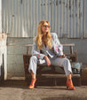 A blonde woman in a gray suit sitting on a Bed Stu Brie II wooden bench.