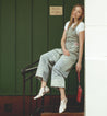 A woman in Bed Stu overalls sitting on the steps of a building.