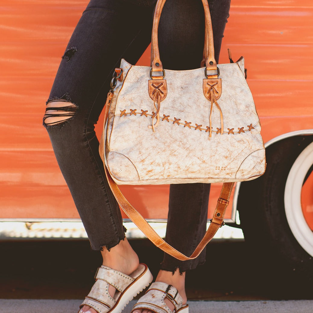 A woman carrying a white and tan Bed Stu Bruna leather bag.