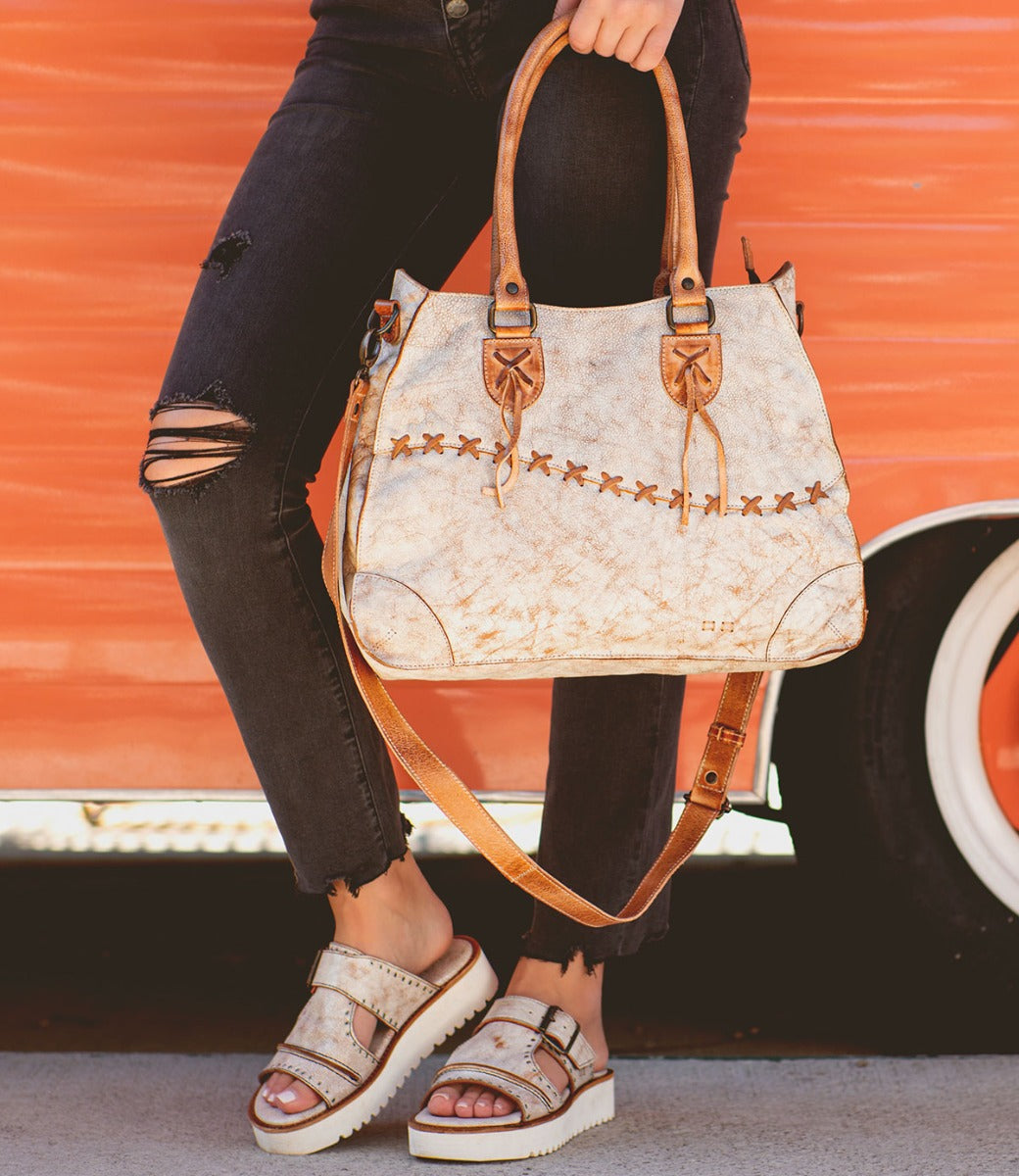 A woman carrying a white and tan Bed Stu Bruna leather bag.