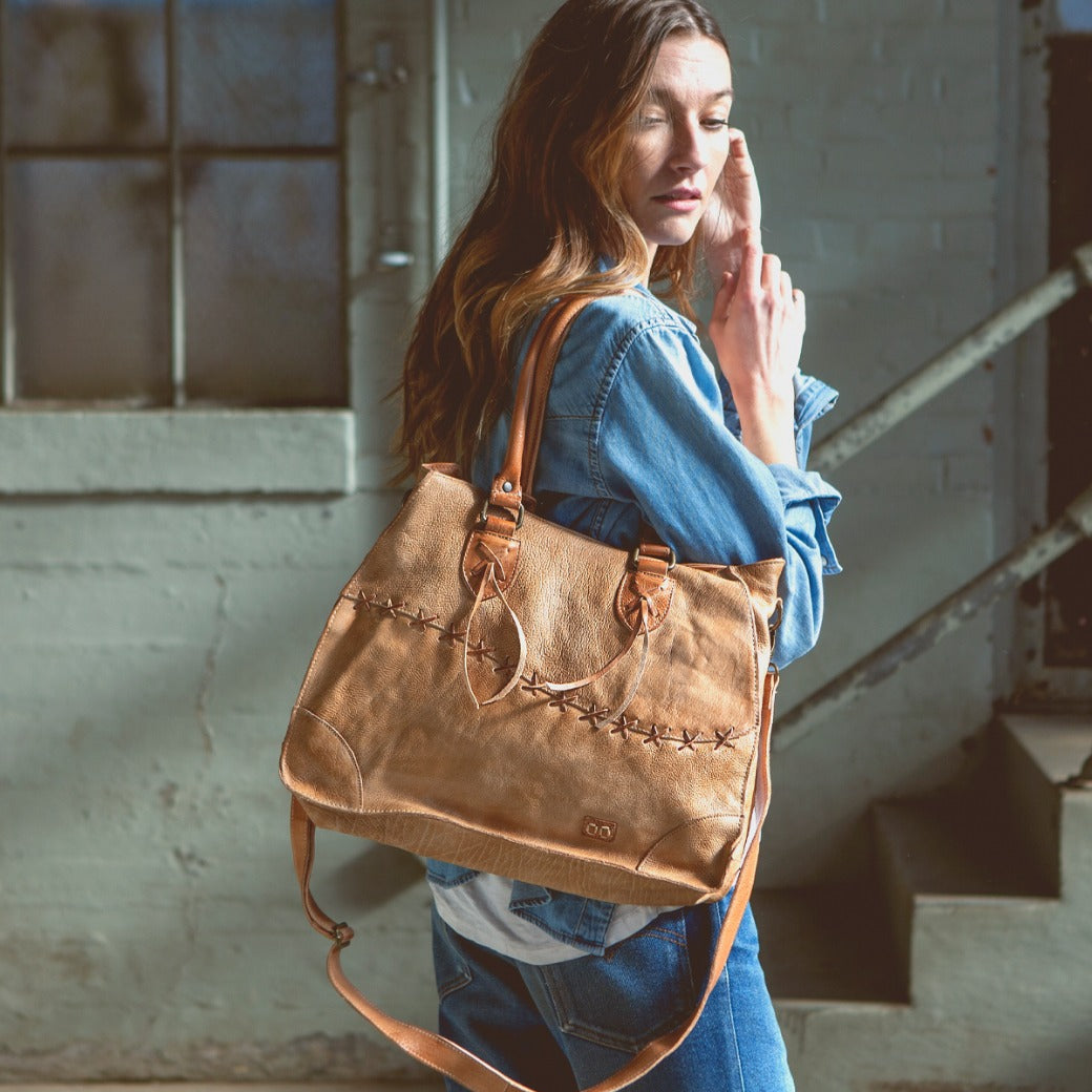 A woman holding a Bed Stu Bruna tan leather bag.