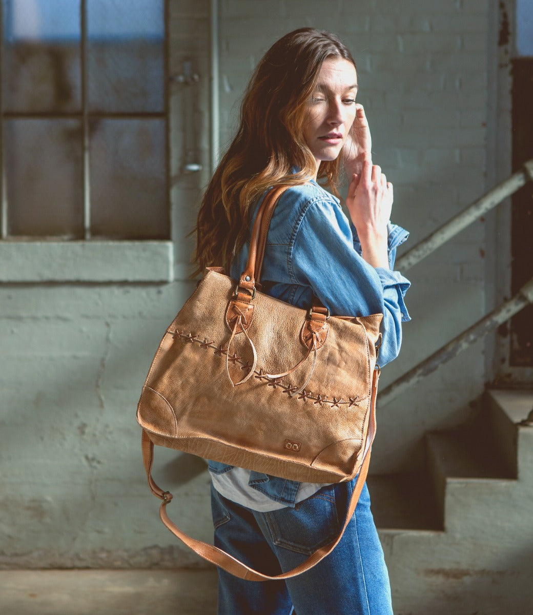 A woman holding a Bed Stu Bruna tan leather bag.