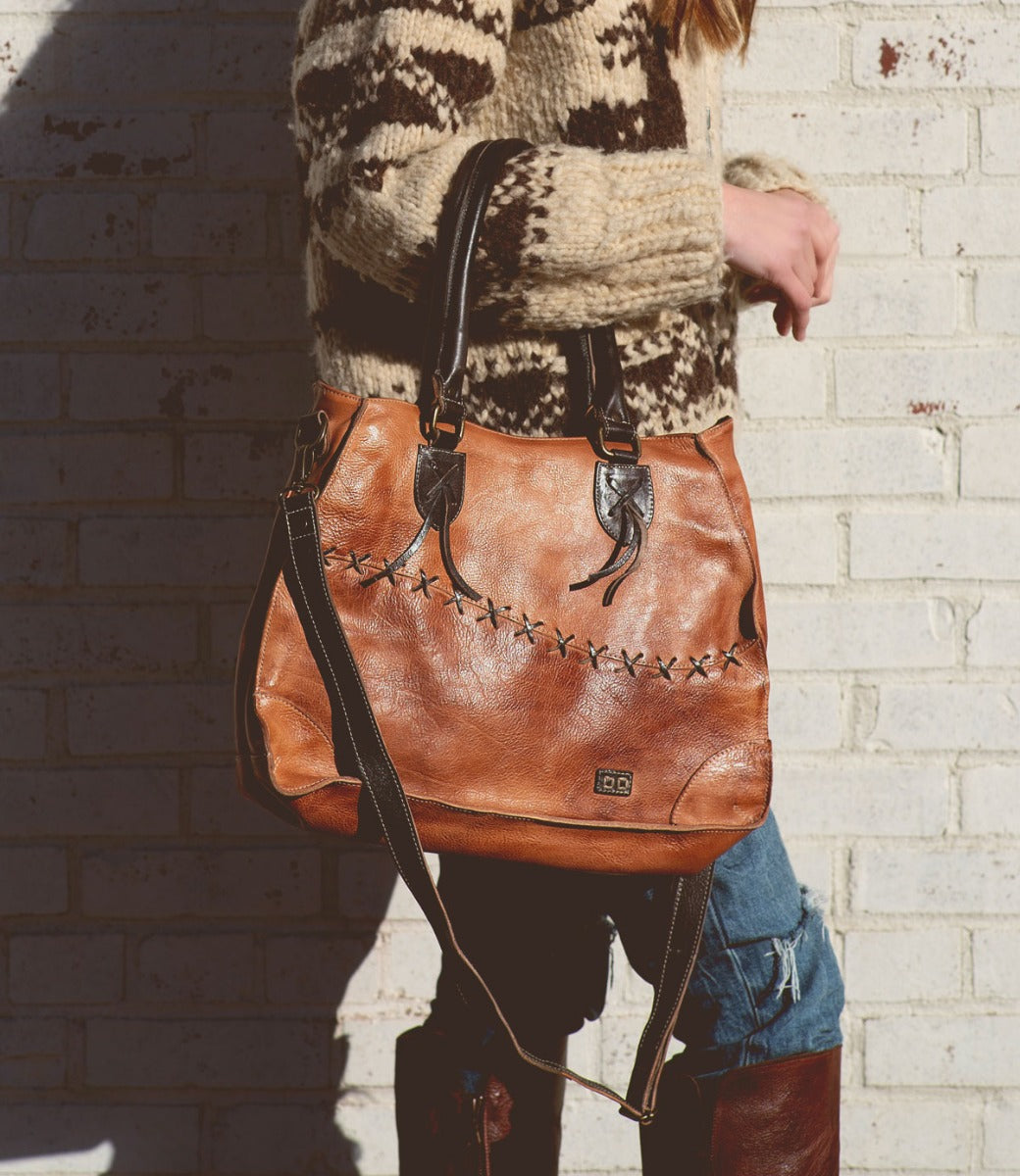 A woman carrying a tan Bed Stu Bruna pure leather bag with black straps.