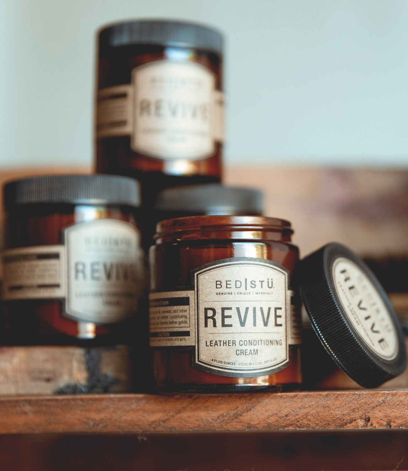 Four jars of Bed Stu Revive Leather Cream sitting on a wooden table.