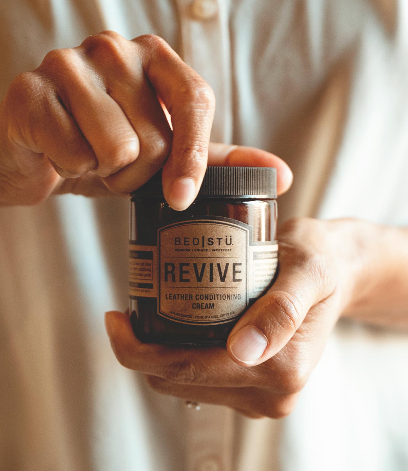 A person holding a jar of Revive Leather Cream (Bed Stu).