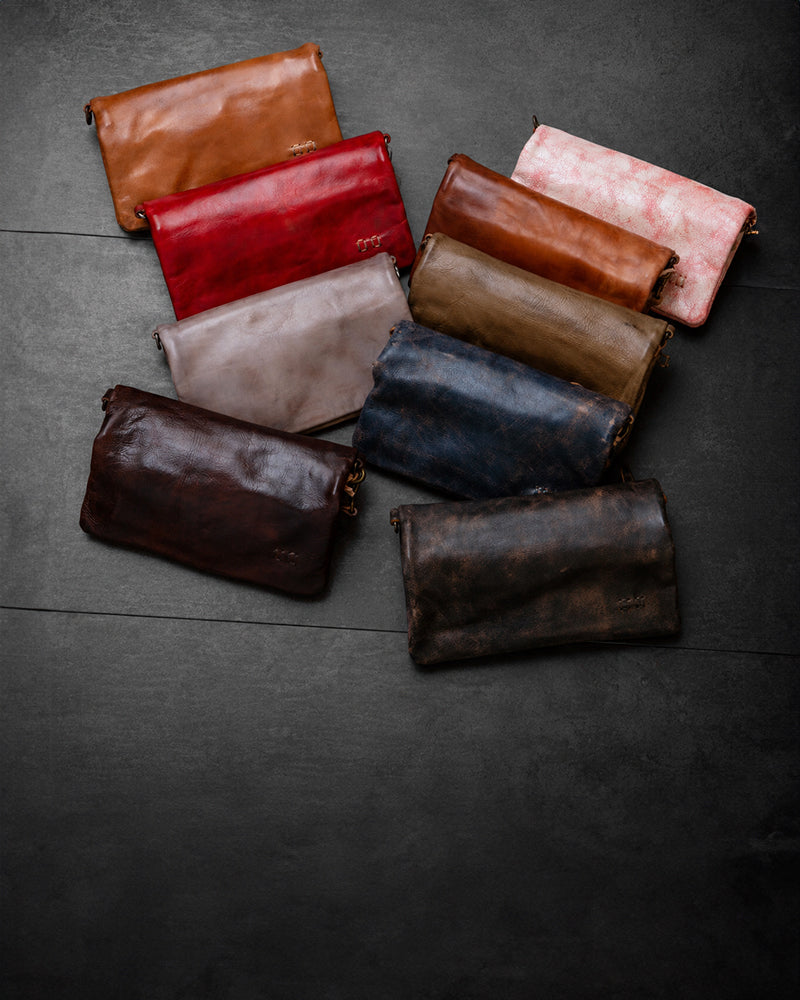 A group of leather clutch bags in assorted colors is arranged on a dark surface.