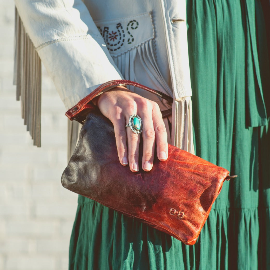 A woman in a green dress holding a Bed Stu Cadence clutch.