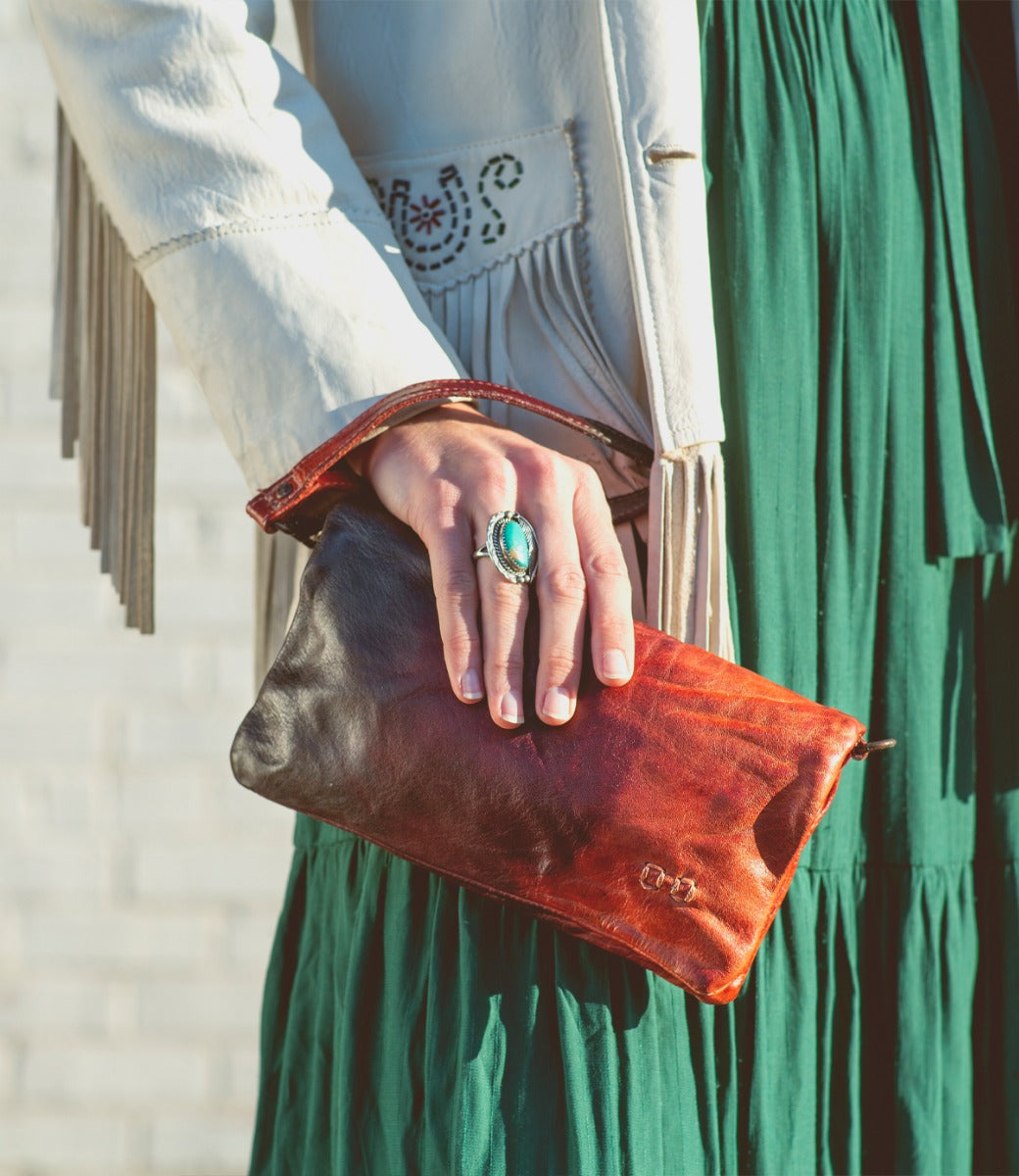 A woman in a green dress holding a Bed Stu Cadence clutch.