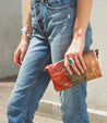 A woman holding a Bed Stu Cadence multi-colored leather clutch.