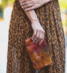 A woman in a leopard print dress holding a Bed Stu Cadence clutch.