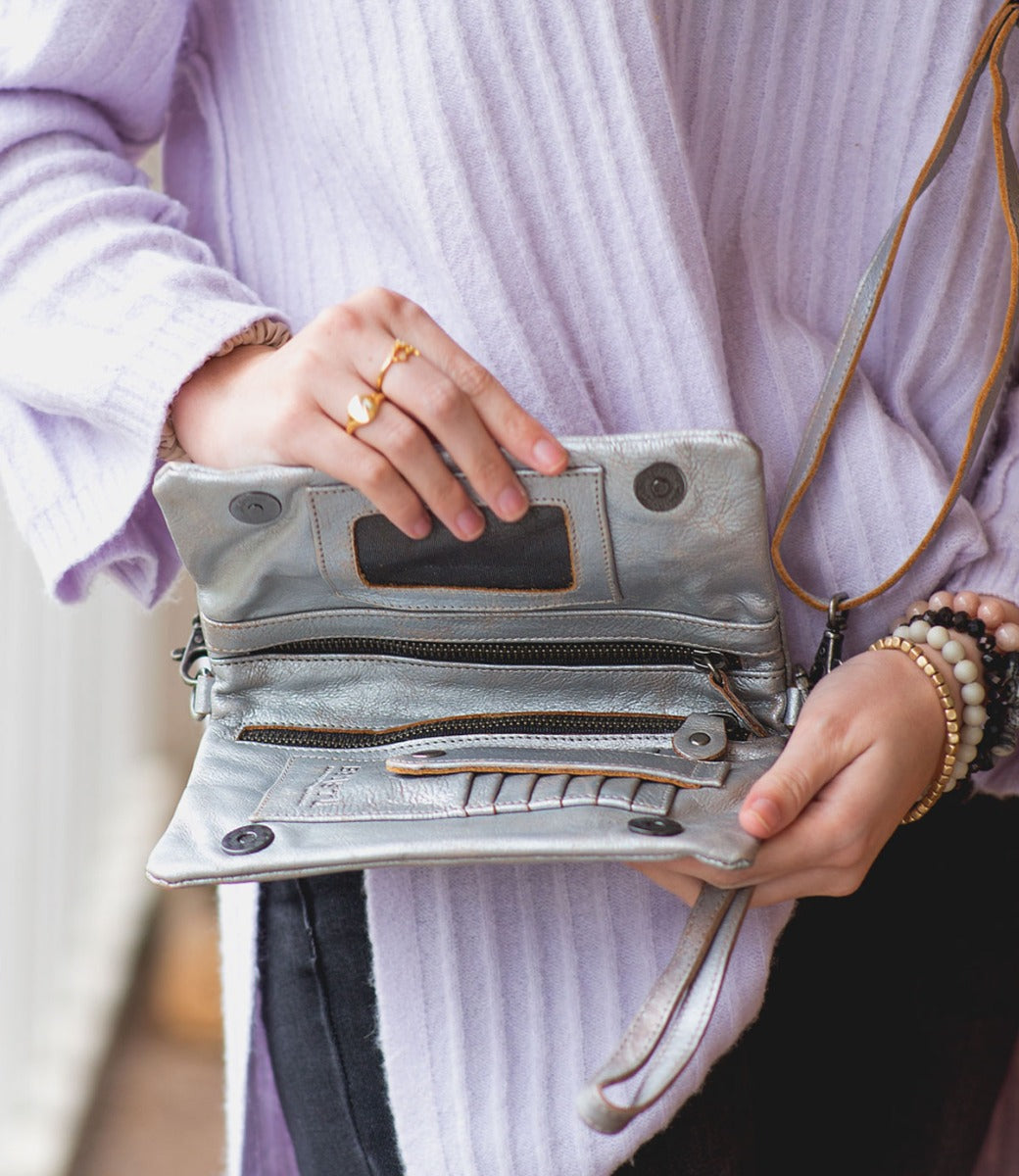A woman wearing a purple sweater holding a silver Bed Stu Cadence purse.