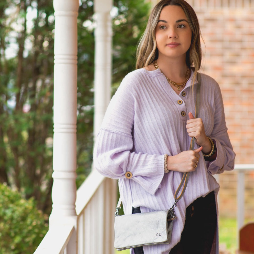 A woman wearing a Bed Stu Cadence silver leather clutch.