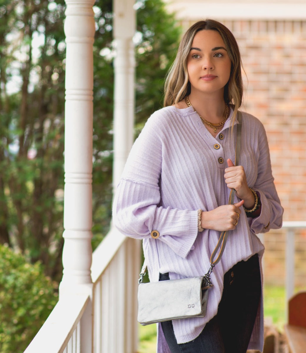 A woman wearing a Bed Stu Cadence silver leather clutch.