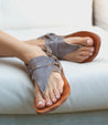 A woman wearing a pair of Bed Stu Callista sandals on a couch.