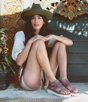 A woman in a Camden hat and Bed Stu sandals sitting on the ground.