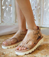 A woman wearing Bed Stu Camden sandals on a rug.