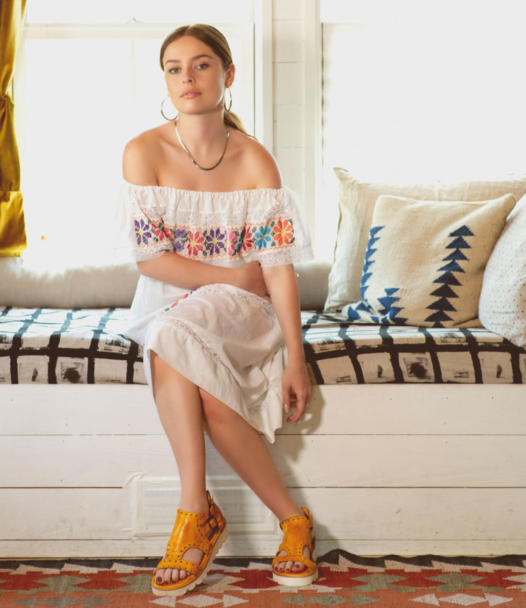 A young woman in a white dress sitting on a Bed Stu Camden couch.