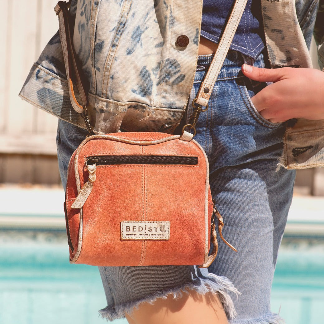 A woman is standing next to a pool holding a Bed Stu Capture bag.