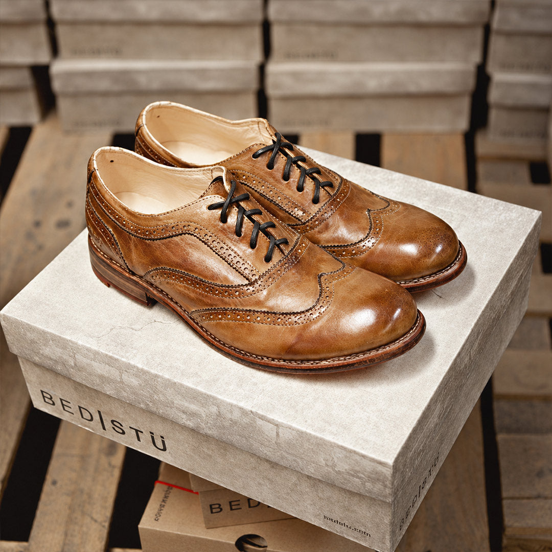 Tan leather wingtip oxfords with black laces, resting on a Bed Stu shoebox.