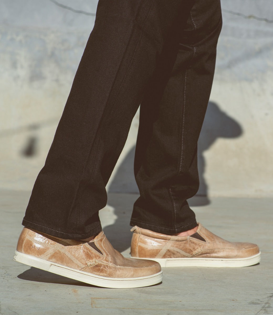 A person wearing a pair of Bed Stu Carp tan slip-on shoes.