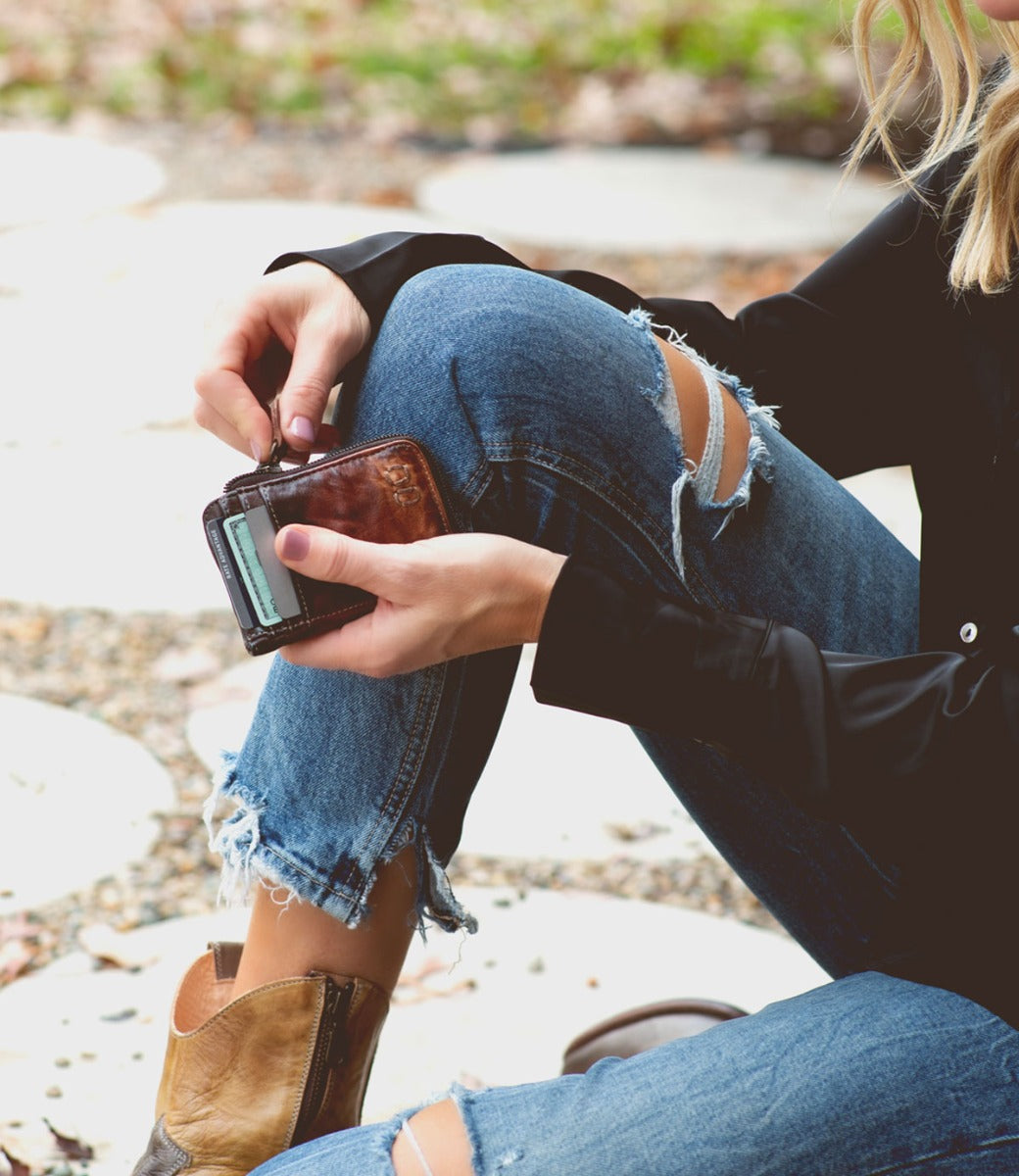 A woman sitting on the ground holding a Carrie cell phone by Bed Stu.