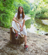 A woman is sitting on a Carrington stump next to a river by Bed Stu.