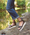 A woman standing on a rock next to a river wearing Bed Stu sandals.