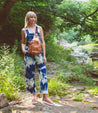 A woman in a jumpsuit wearing Caroll sandals by Bed Stu, standing near a river.