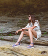 A woman is sitting on a rock and wearing Bed Stu sandals, called Carroll.