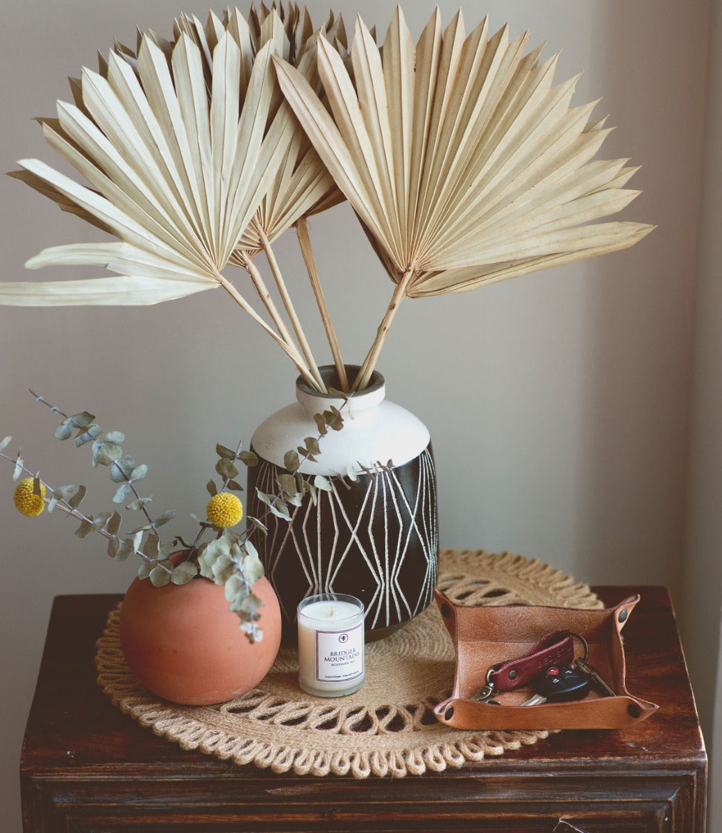 A Bed Stu Expanse vase with palm leaves and a candle on a table.