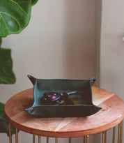A small, square Expanse Catchall Tray by Bed Stu on a wooden table holds a set of car keys and some loose change. A green plant is partially visible in the background.