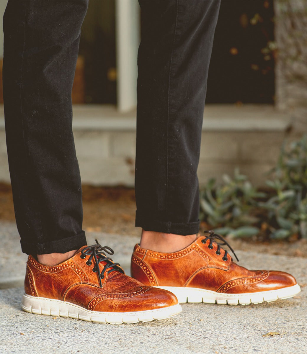 A man wearing a pair of Bed Stu Cayuga II brown wingtip oxford shoes.