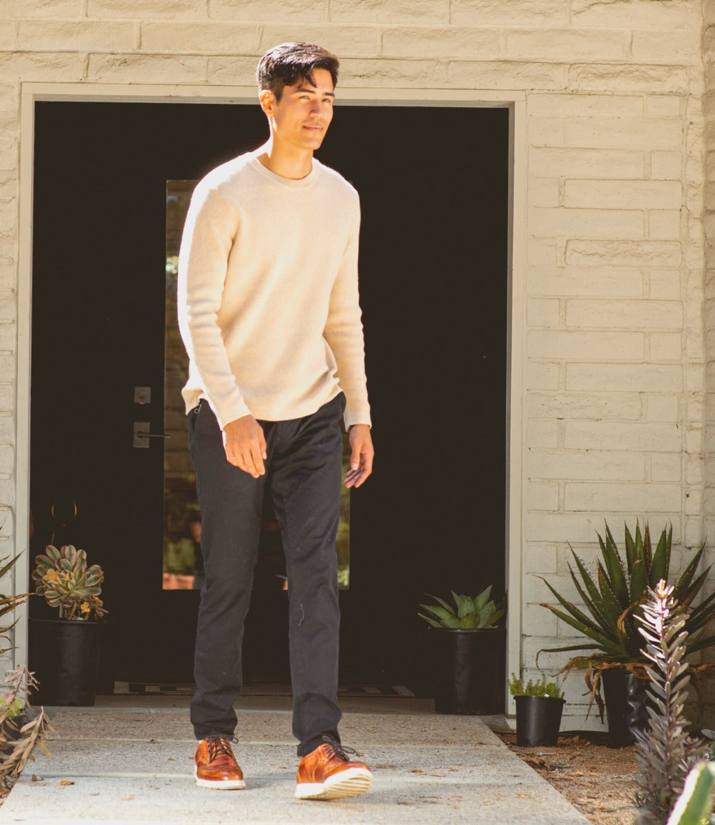 A man in a tan Bed Stu sweater walking into a house.