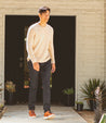 A man in a tan Bed Stu sweater walking into a house.