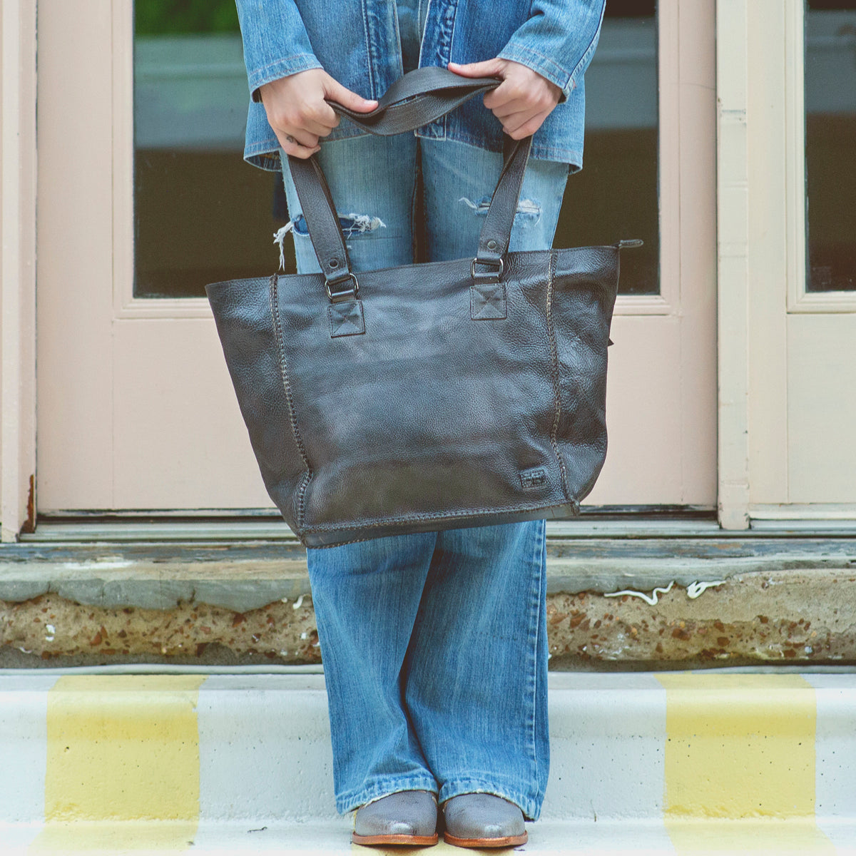 A woman in jeans holding a Bed Stu Celindra LTC tote bag.