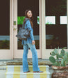 A woman standing on the steps of a house holding a Celindra LTC bag from Bed Stu.