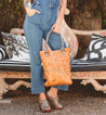 A woman in overalls holding a Bed Stu Celta tan tote.