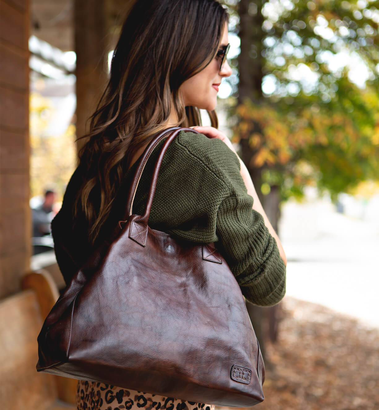 A woman carrying a Cersei brown leather tote bag by Bed Stu.