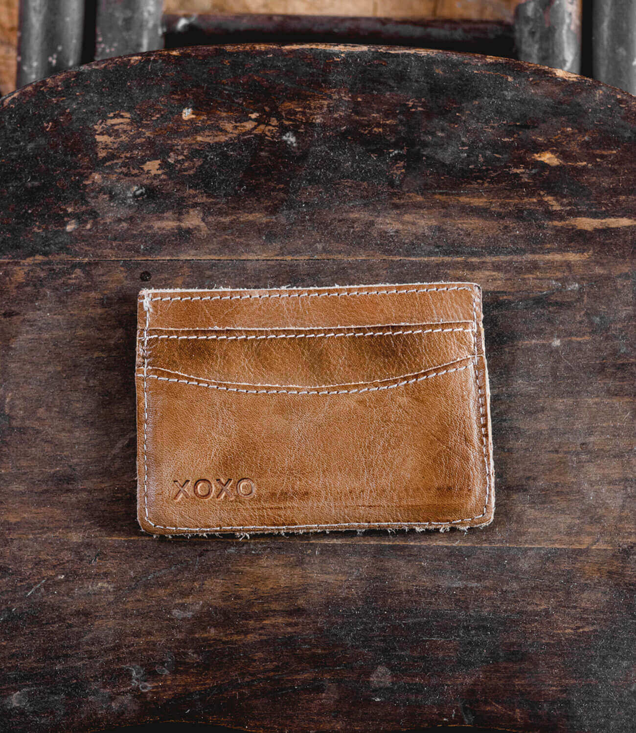 A brown leather Chuck card holder sitting on top of a wooden chair, made by Bed Stu.