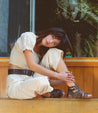 A woman sitting on a wooden bench with Bed Stu Claire III sandals.