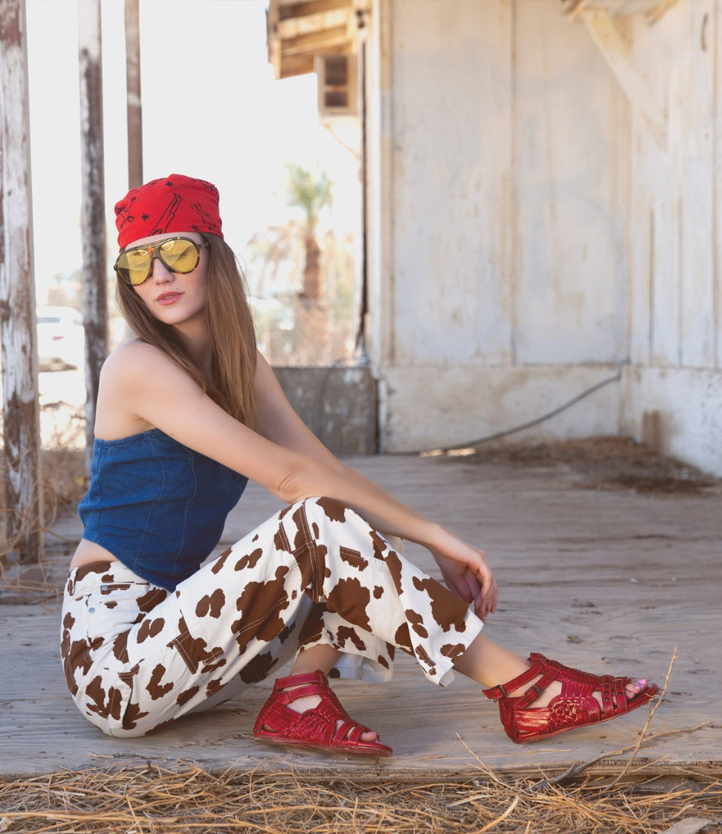 A woman wearing Bed Stu cow print pants and a Bed Stu red hat.