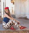 A woman wearing Bed Stu cow print pants and a Bed Stu red hat.