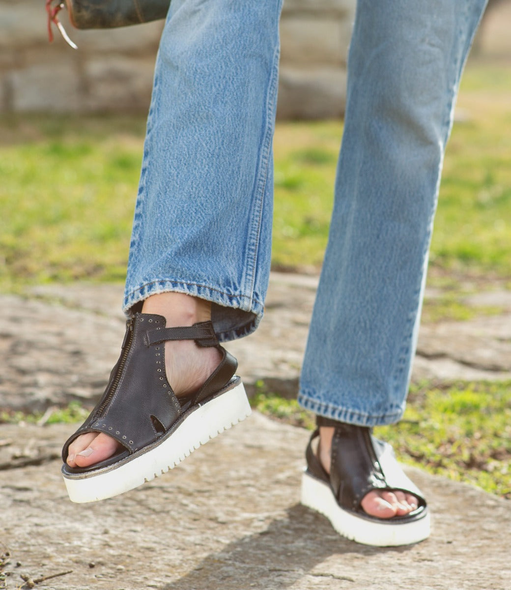A person wearing Clancy sandals by Bed Stu, made of tan leather with a white sole.