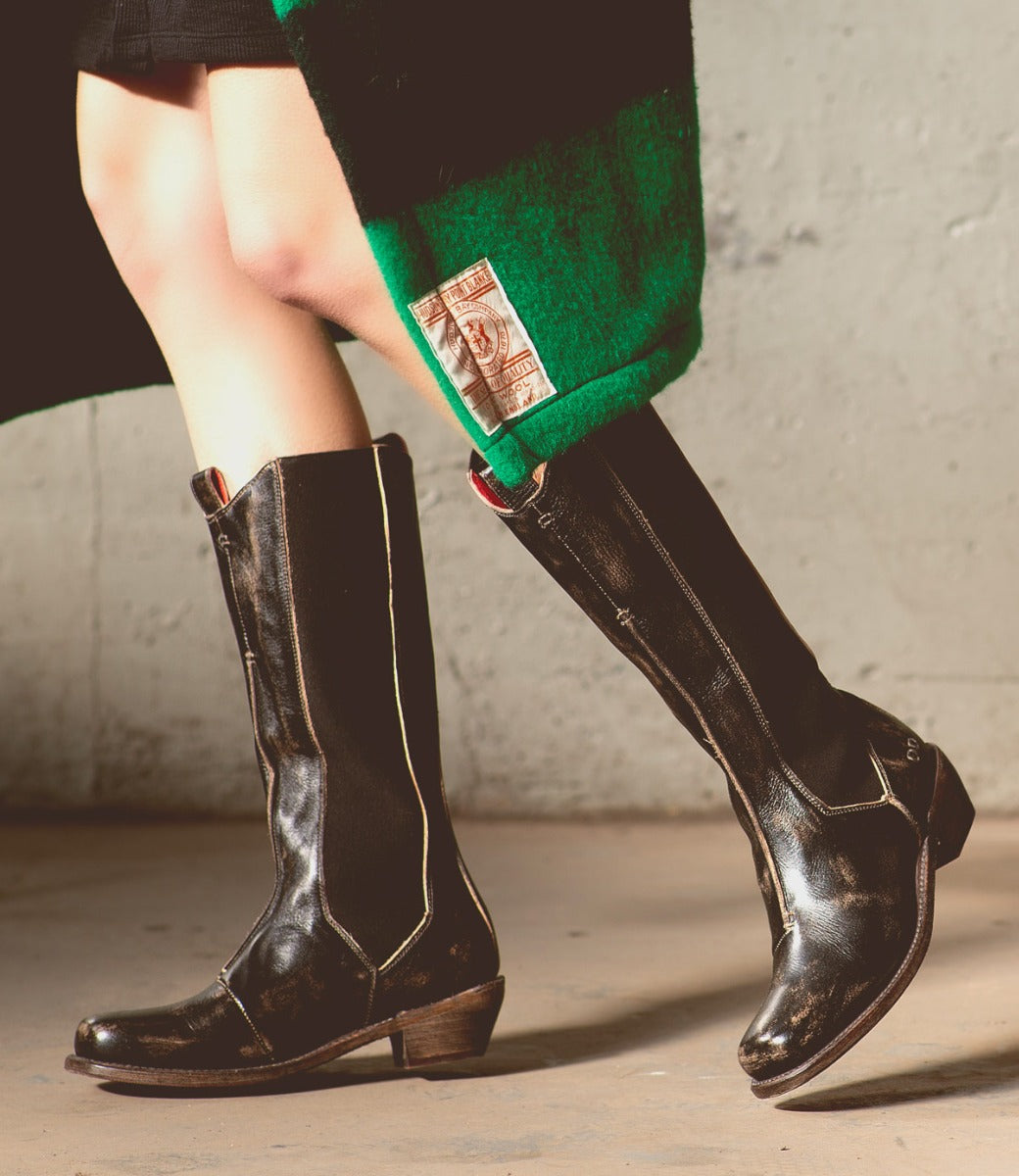 A woman wearing black Clarisse boots and a green Bed Stu coat.