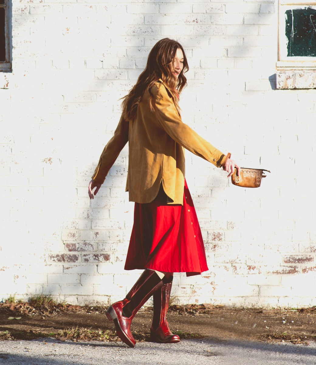 A woman in a red dress walking with a Clarisse boots from the brand Bed Stu.