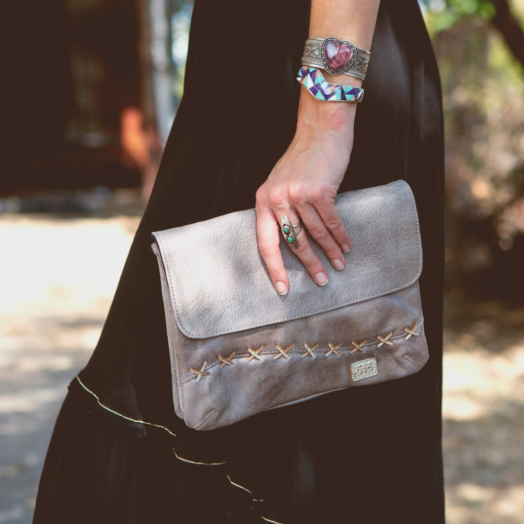 A woman wearing a black dress holding a Bed Stu Cleo clutch.