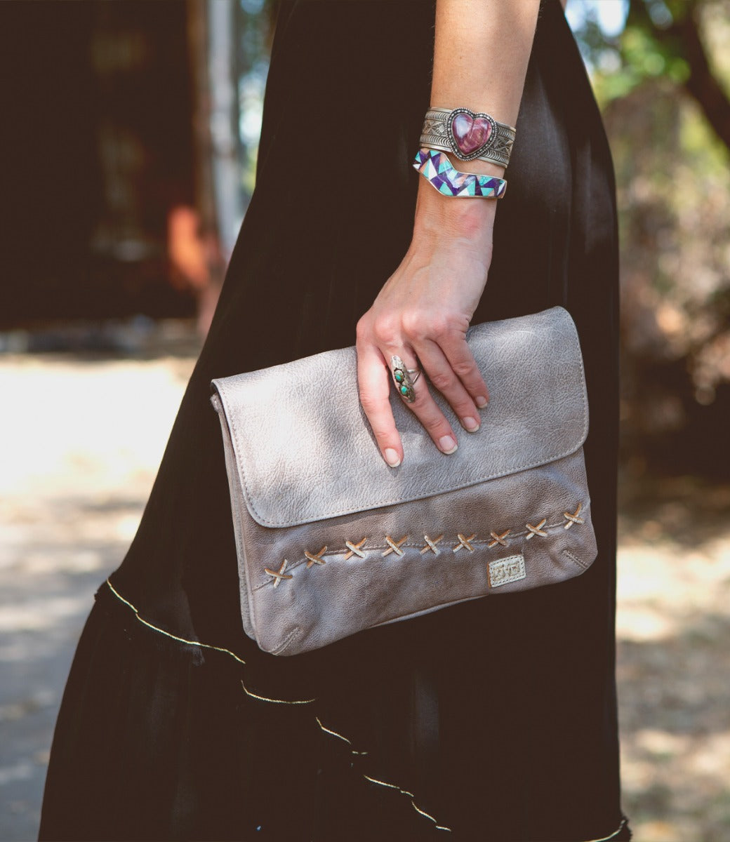 A woman wearing a black dress holding a Bed Stu Cleo clutch.