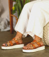 A woman's feet are sitting on a pair of Bed Stu Crawler sandals.