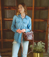 A woman wearing Bed Stu jeans and a Bed Stu denim shirt standing in a barn.