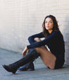 A woman sitting on the sidewalk in Bed Stu Della boots.